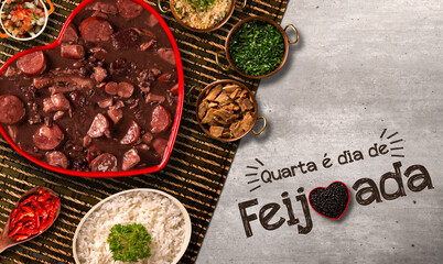 Fototapeta na wymiar Brazilian Feijoada Food in red heart bowl. Written Wednesday is feijoada day in Portuguese. Top view.