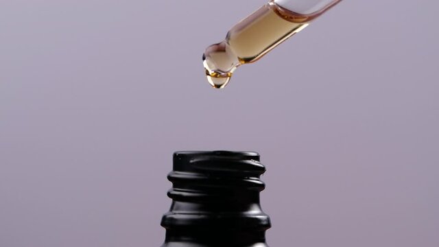 Essential oil dropping from glass dropper into bottle in slow motion