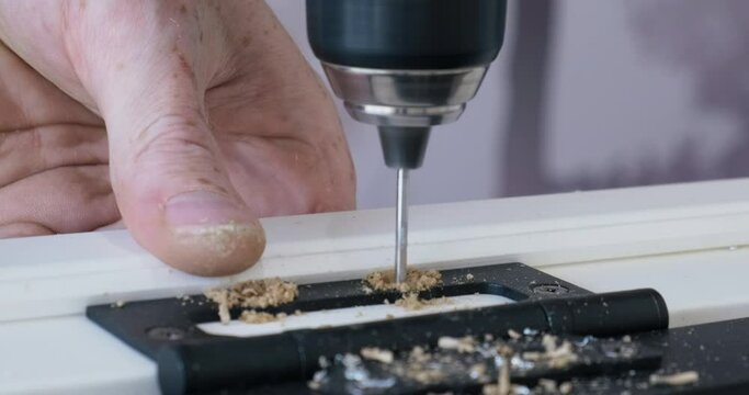 Close-up Drill. Master Drills Holes in Wooden Board. Fasteners Door Hinges to Door. Work on Installing Doors in House. Repair work in Room. Men's Hands Closeup. Sawdust. Black Door Hinges. Hand Work