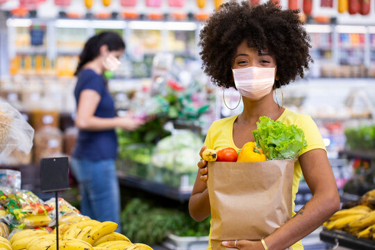 Healthy positive happy african woman using mask, holding a paper shopping bag full of fruit and vegetables