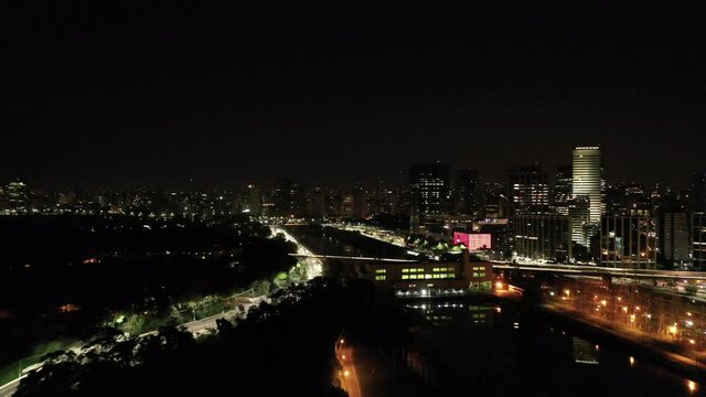 Establishing shot of the skyline of São Paulo city by night. Drone traveling in approaching the Pinheiros River.