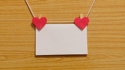 Mockup photo frame with two red hearts, empty space for text. Blank paper with hearts and clothespins hanging on a rope