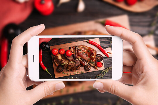 Blogger taking picture of delicious roasted ribs at table, closeup. Food photography