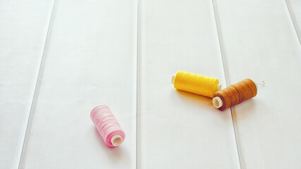 Naklejka premium Three reels of threads lie on a table of light wood.