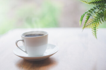 white ceramic cup of hot coffee on wooden table with blurred background in soft focus