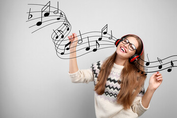 Young woman listening to music with headphones on grey background