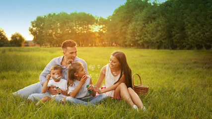 Happy family having picnic and blowing soap bubbles in park at sunset