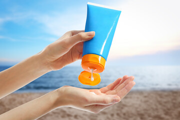 Young woman applying sun protection cream near sea, closeup