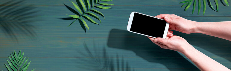 Smartphone with tropical palm leaves and shadow - flat lay