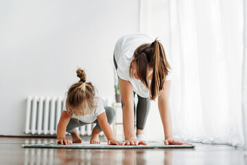 Happy mom and little daughter doing morning exercise together at bright interior of home