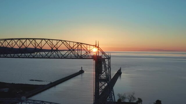 Aerial view of sunset through metal framework of ferry lift bridge in Duluth Minnesota - drone tracking shot