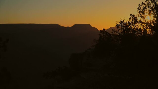 Timelapse tourists take pictures of grand canyon from high ledge against sunrise silhouette