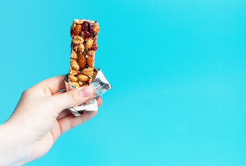 A woman's hand holds a cereal bar on a blue background, copy of the space