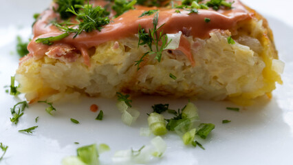 A portion of potato casserole with sauce and herbs on a white plate