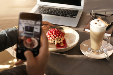 Young blogger taking picture of dessert at table in cafe, closeup