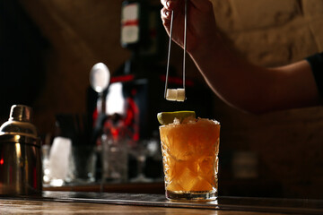Bartender decorating glass of fresh alcoholic cocktail at bar counter, closeup. Space for text