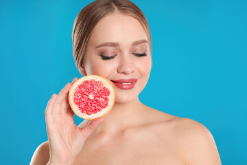 Young woman with cut grapefruit on blue background. Vitamin rich food