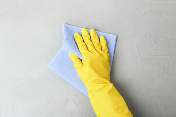 Person in gloves wiping grey table with rag, top view