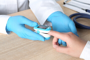 Doctor examining patient with modern fingertip pulse oximeter at wooden table, closeup