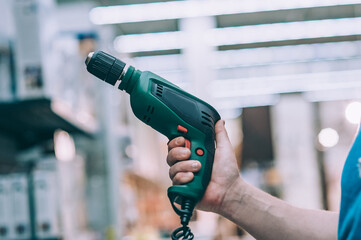 A man holds an electric drill in his hand for drilling. A buyer in a hardware store selects a...