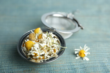 Dry chamomile flowers in infuser on light blue wooden table, closeup