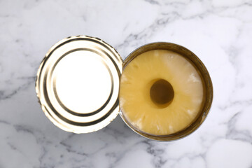 Tin with canned pineapple on white marble table, top view
