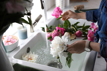 Woman with beautiful peonies near kitchen sink, closeup