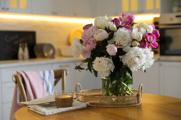 Beautiful peonies and cup of coffee on wooden table in kitchen
