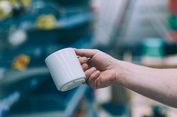 Mockup mug in a man hand, against the background of shop windows.