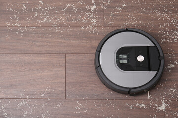 Removing groats from wooden floor with robotic vacuum cleaner at home, top view. Space for text