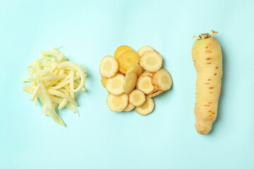 Whole and cut raw white carrots on light blue background, flat lay