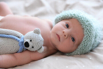 Cute newborn baby in warm hat with toy lying on bed