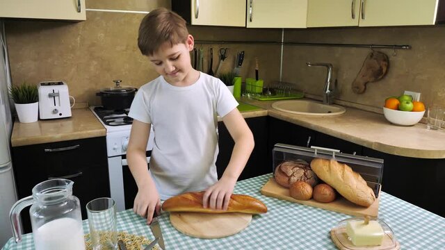 Boy cuts bread with knife on the kitchen table
