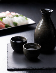 Sake and sashimi on a black background - obrazy, fototapety, plakaty