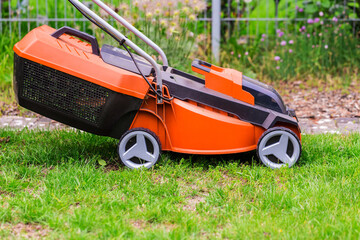 Obraz na płótnie Canvas Electric mower cutting green grass in backyard. Gardening background.