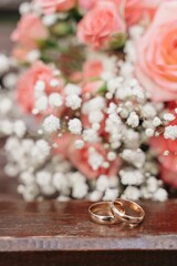 A couple of golden wedding rings on dark wooden branch with bride's bouquet on background, soft focus, roses