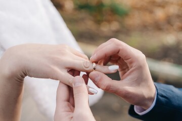 Close up of wedding hands: groom is putting on a golden ring on a bride's finger