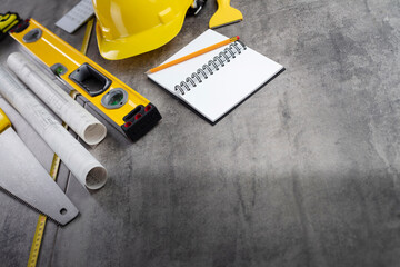 Fototapeta premium Contractor concept. Tool kit of the contractor: yellow hardhat, libella, hand saw. Plans and notebook on the gray tiles background.