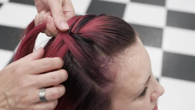 Professional hairdresser plaiting braids to red colored female hair