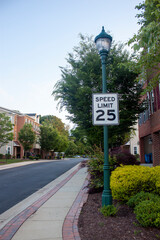 Image shows a road sign saying speed limit 25 mph. Sign is attached to a street lamp. Photo was taken at a residential neighborhood on a street that runs between townhouses where kids might be playing