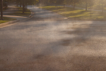 Heavy shower followed by sunshine causes rain puddles to evaporate on asphalt on a hot summer day. Image shows water transitioning to vapor all over the street