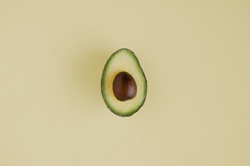 photo of half an avocado on a soft yellow background with  yellow and green flesh and a brown stone