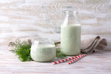 Healthy dietary green kefir (yogurt) with herbs in glass and bottle on wooden table
