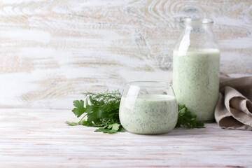 Healthy dietary green kefir (yogurt) with herbs in glass and bottle on wooden table