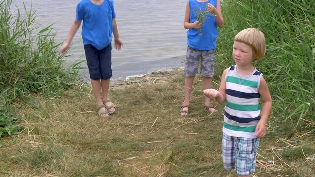 Three boys play and jump on riverbank. Children are happy to go out after quarantine.