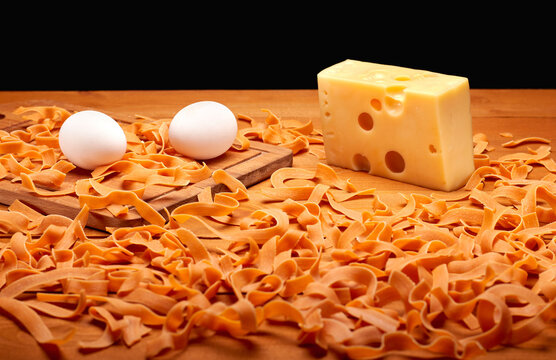 Colorful raw pasta, cheese and eggs on wooden table, healthy food concept
