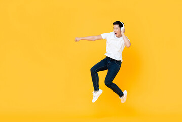 Fototapeta na wymiar Happy handsome young Asian man wearing headphones punching and jumping in colorful yellow background
