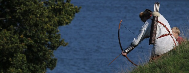 viking in historic costume shooting with longbow and arrows