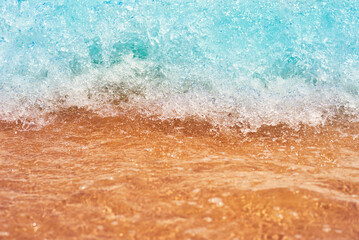 Sea wave on the sand beach, soft focus. Summer background. Waves with splashes and foam