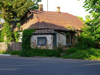 Old clay wooden residential house. Ancient architecture on the streets of modern cities. Forgotten and abandoned house, overgrown with a weaving vineyard